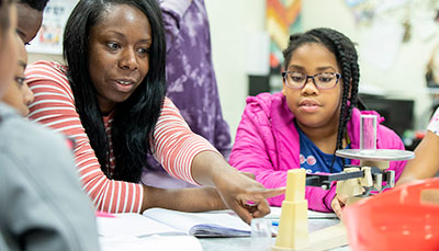 Group of students working together at a table with a student teacher.